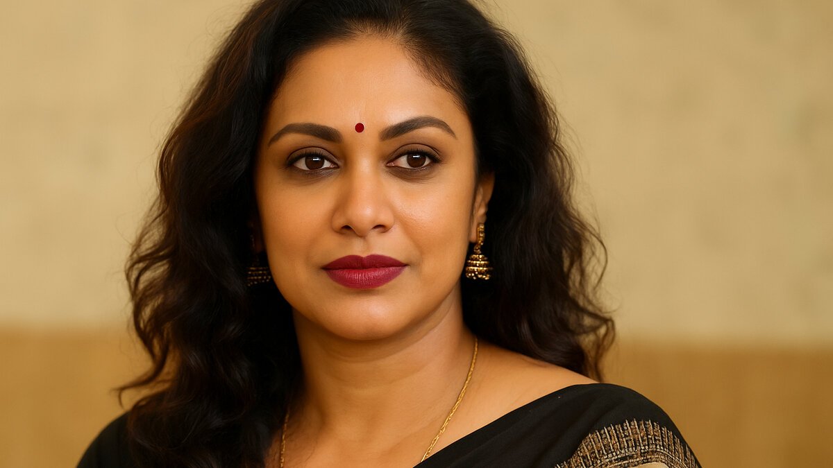 A confident South Asian woman in her late thirties wearing a black and gold sari, gold jhumka earrings, and a small red bindi, with wavy dark hair and bold makeup, standing against a softly blurred beige background.