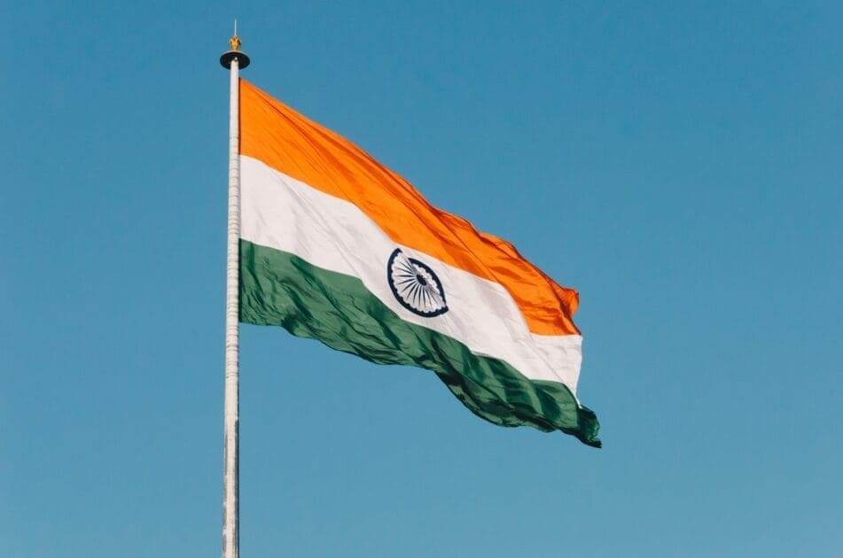 An Indian national flag hanging on a pole, fluttering in the wind against a clear blue sky.